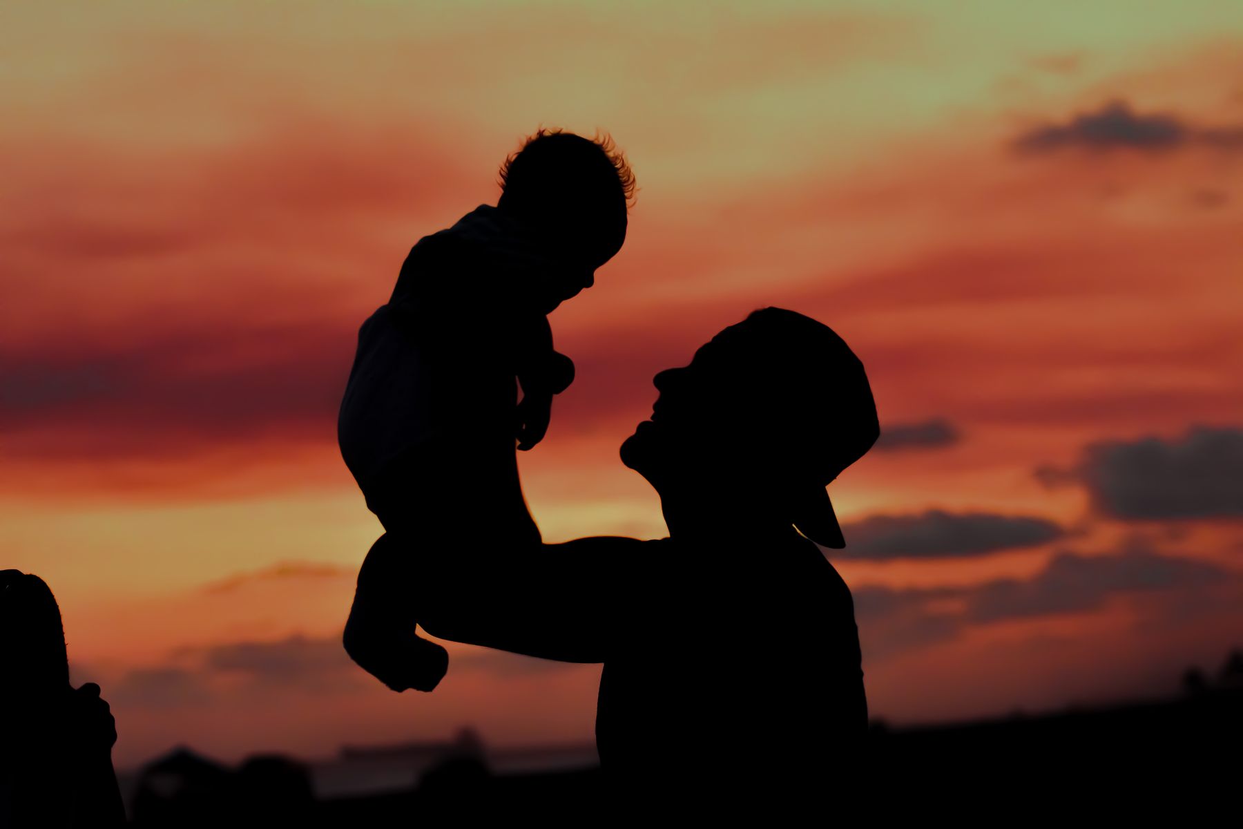 A father lifts his young child into a golden sunset sky, both in joyful silhouette